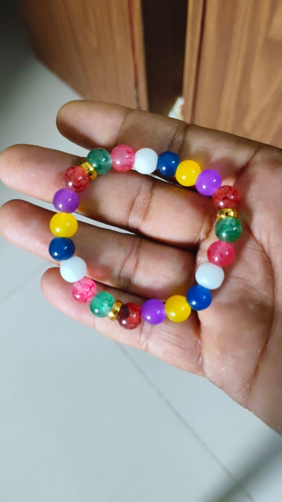 Hand holding a colorful beaded bracelet on a plain background